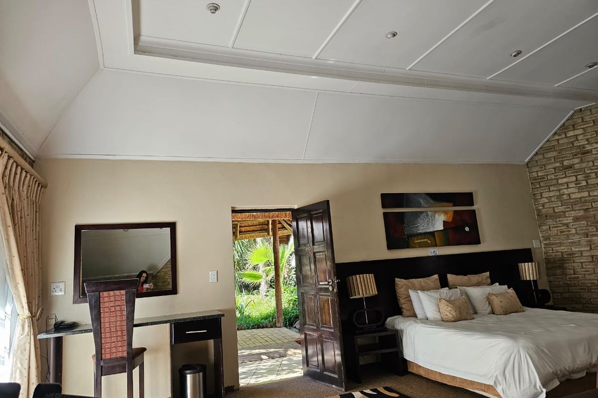 A spacious bedroom featuring a high vaulted ceiling, exposed brick accent wall, and direct access to an outdoor patio area.