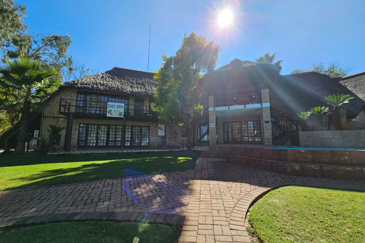 Exterior view of a multi-level office property featuring a thatched roof, brick facade, paved walkways, and a landscaped garden area.