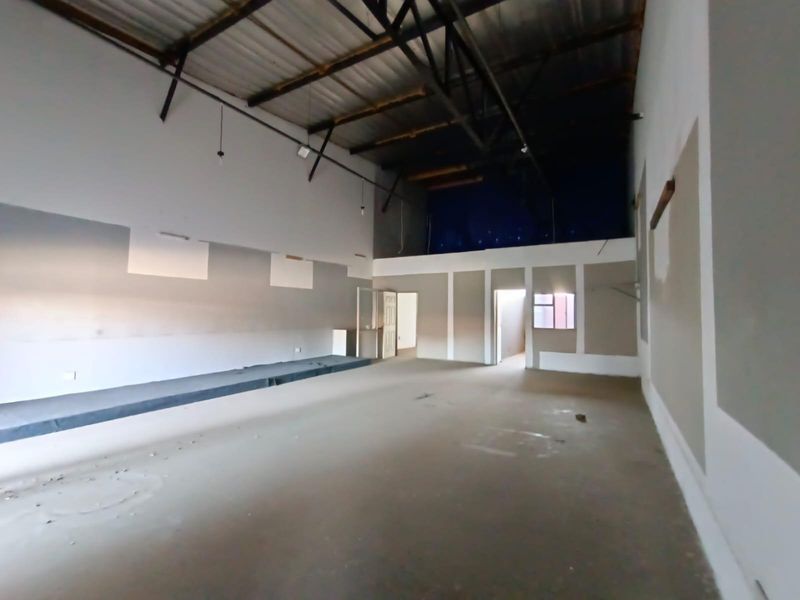 A large, open-plan commercial space featuring high exposed ceilings, unfinished drywall, and concrete flooring, suitable for a variety of business or industrial uses.
