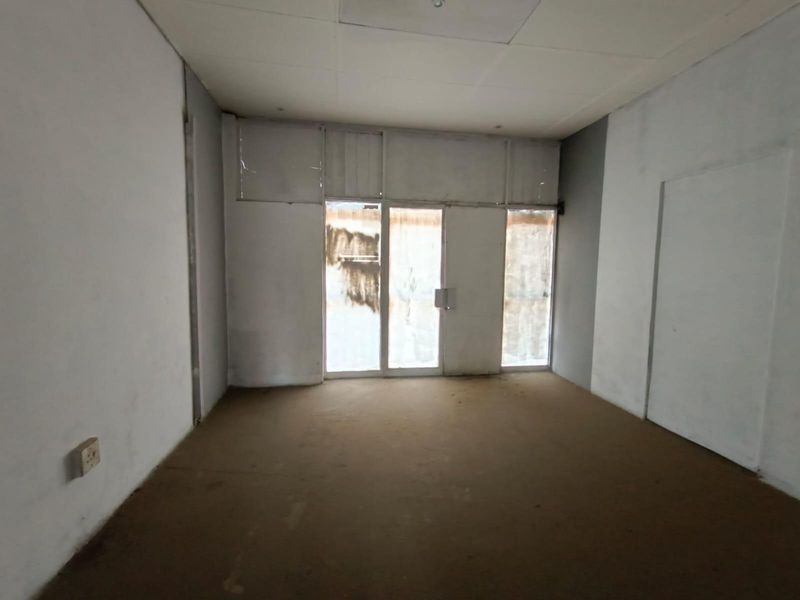 An empty commercial office space featuring large glass entrance doors, neutral walls, and worn flooring, offering a blank canvas for renovation.