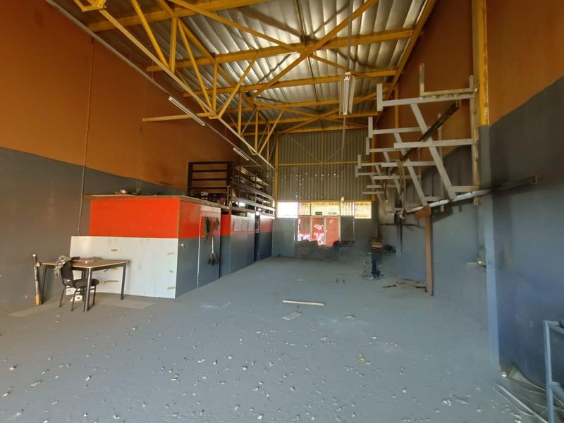 Spacious industrial warehouse unit featuring high exposed steel truss ceilings, concrete flooring, and built-in storage racking systems.