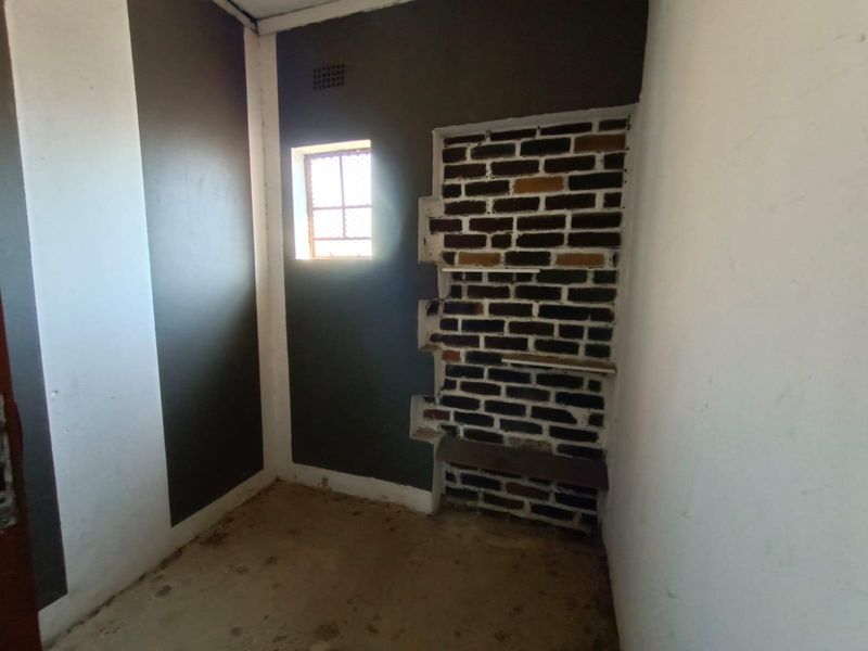A small, unfinished utility room featuring exposed brickwork shelving and a small window, requiring renovation to improve its functional state.