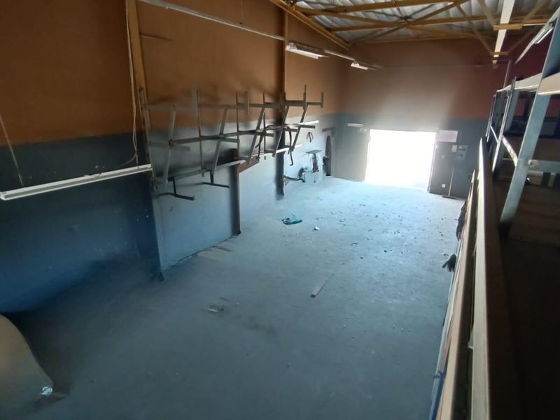 An industrial warehouse or utility space featuring high ceilings, exposed steel trusses, wall-mounted storage racks, and a concrete floor.