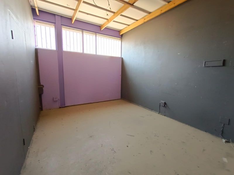 An empty, unfinished utility space featuring exposed timber ceiling beams, high-level security windows, and raw concrete flooring, suitable for renovation or storage.