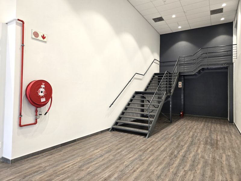 Modern office space featuring a sleek metal staircase, wood-look laminate flooring, and integrated fire safety equipment in a clean, minimalist setting.