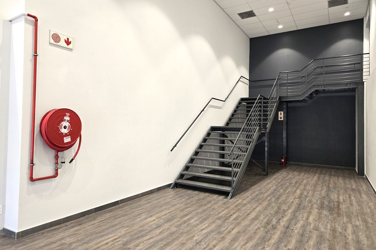 Modern office space featuring a sleek metal staircase, wood-look laminate flooring, and integrated fire safety equipment in a clean, minimalist setting.