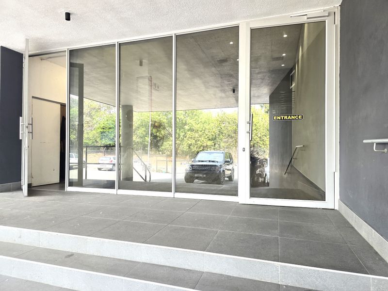 Modern office building entrance featuring large glass doors, tiled steps, and a clean, professional facade.