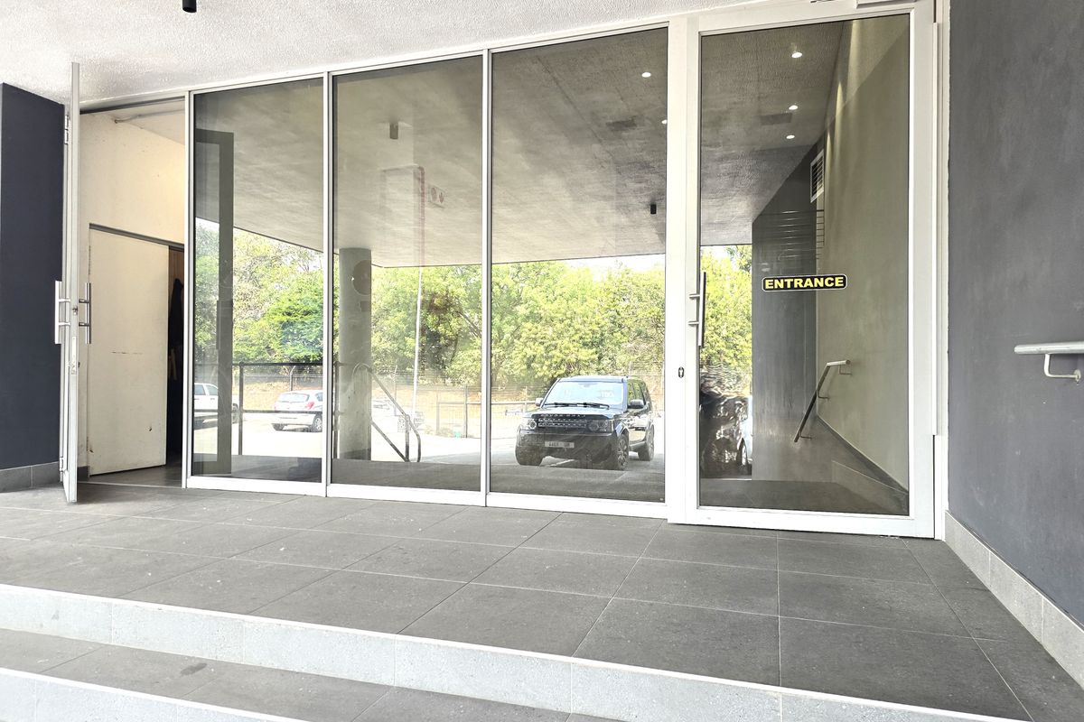 Modern office building entrance featuring large glass doors, tiled steps, and a clean, professional facade.