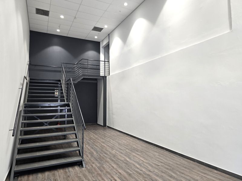Modern office interior featuring a sleek metal staircase, high ceilings with recessed lighting, and durable laminate flooring in a clean, open-plan layout.