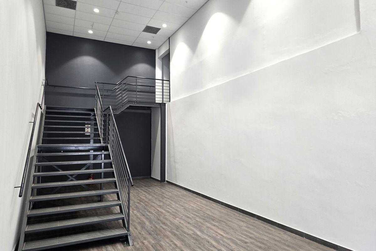 Modern office interior featuring a sleek metal staircase, high ceilings with recessed lighting, and durable laminate flooring in a clean, open-plan layout.