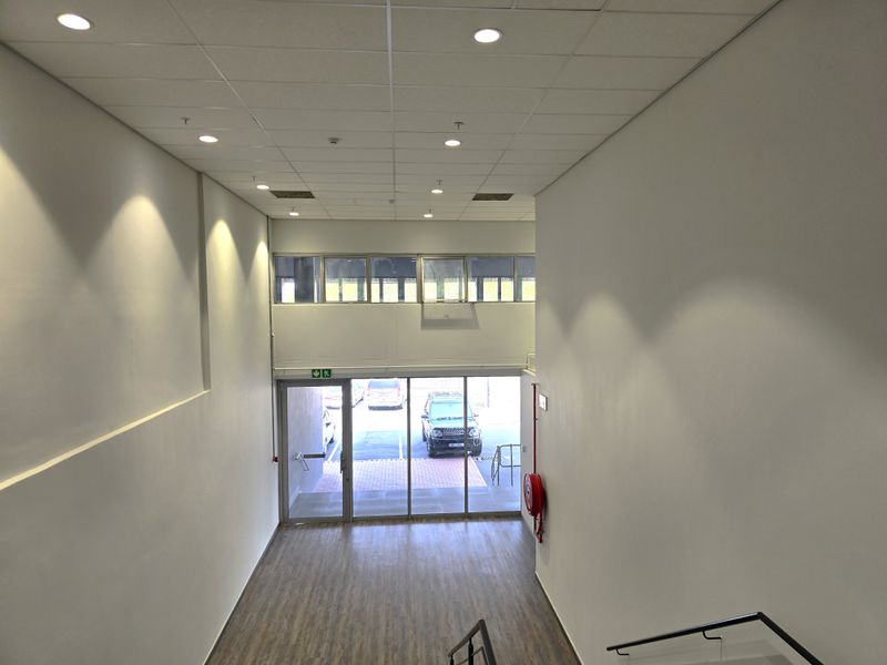 Spacious office entrance area featuring high ceilings, recessed lighting, laminate flooring, and a glass-fronted entry door with natural light.