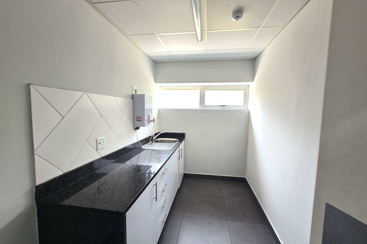 A clean, functional kitchenette featuring granite countertops, white cabinetry, a stainless steel sink, and tiled finishes, suitable for office use.