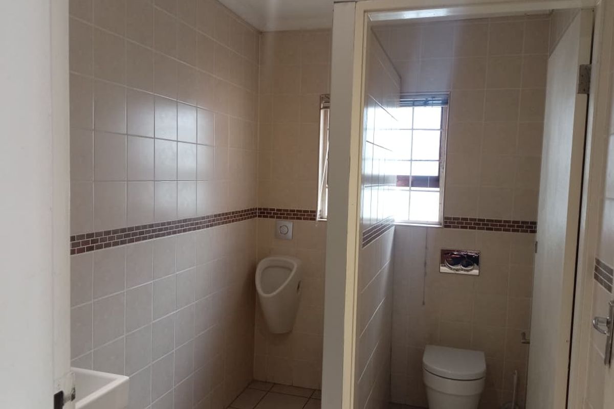 A functional office restroom featuring a wall-mounted urinal, a modern wall-hung toilet, and tiled wall finishes.