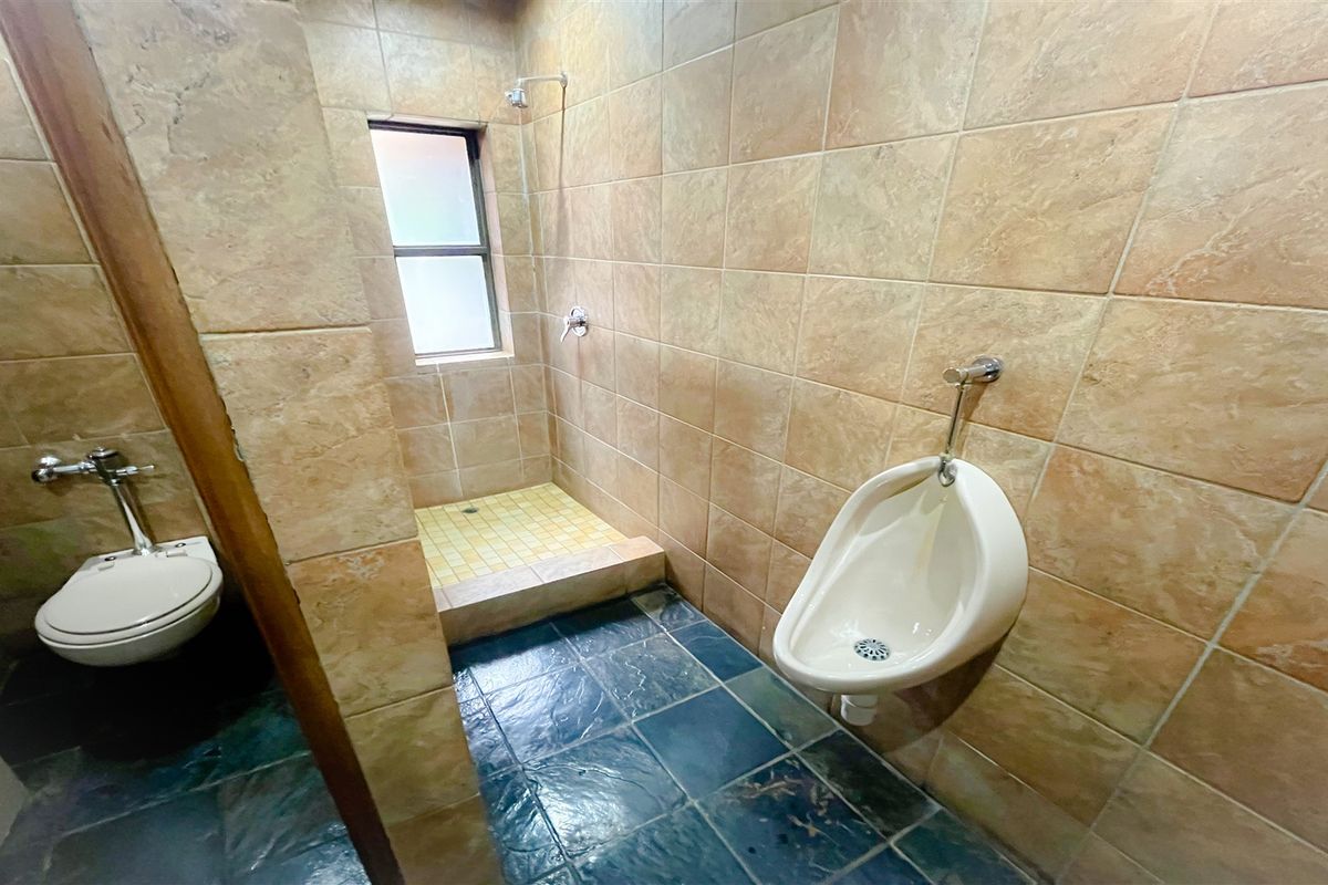 A functional office restroom featuring a wall-mounted urinal, a standard toilet, and a tiled shower stall with a window.