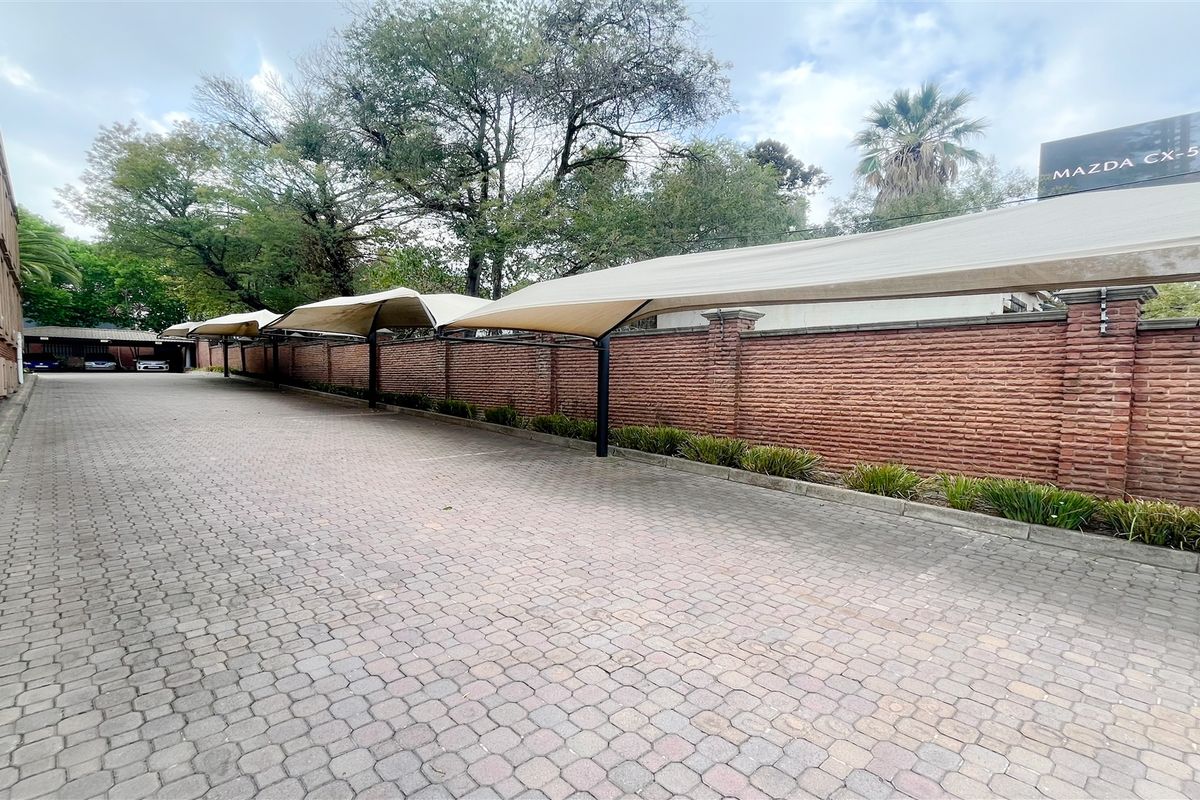 A paved outdoor parking area featuring a long row of covered shade-cloth carports and a decorative brick boundary wall.