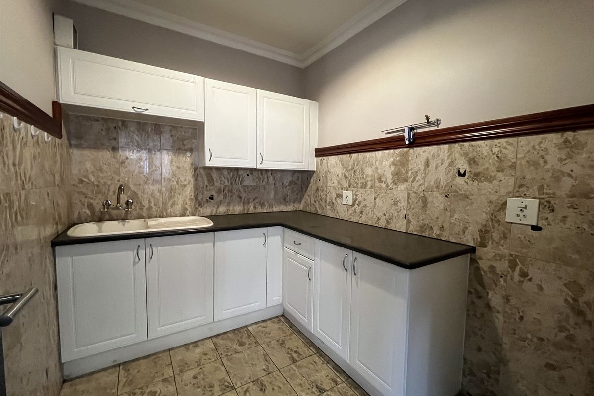 A functional kitchenette area featuring white cabinetry, dark countertops, a single basin sink, and marble-style wall tiling.