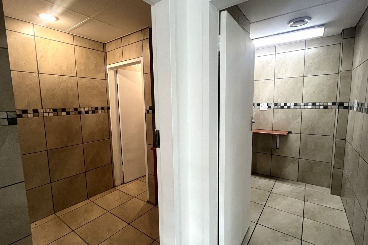 A view of two adjacent office restroom or utility spaces featuring full-height wall tiling, tiled flooring, and built-in shelving.