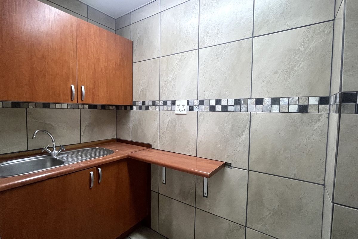 A functional kitchenette area featuring wood-look cabinetry, a stainless steel sink, and tiled walls with a decorative mosaic border.