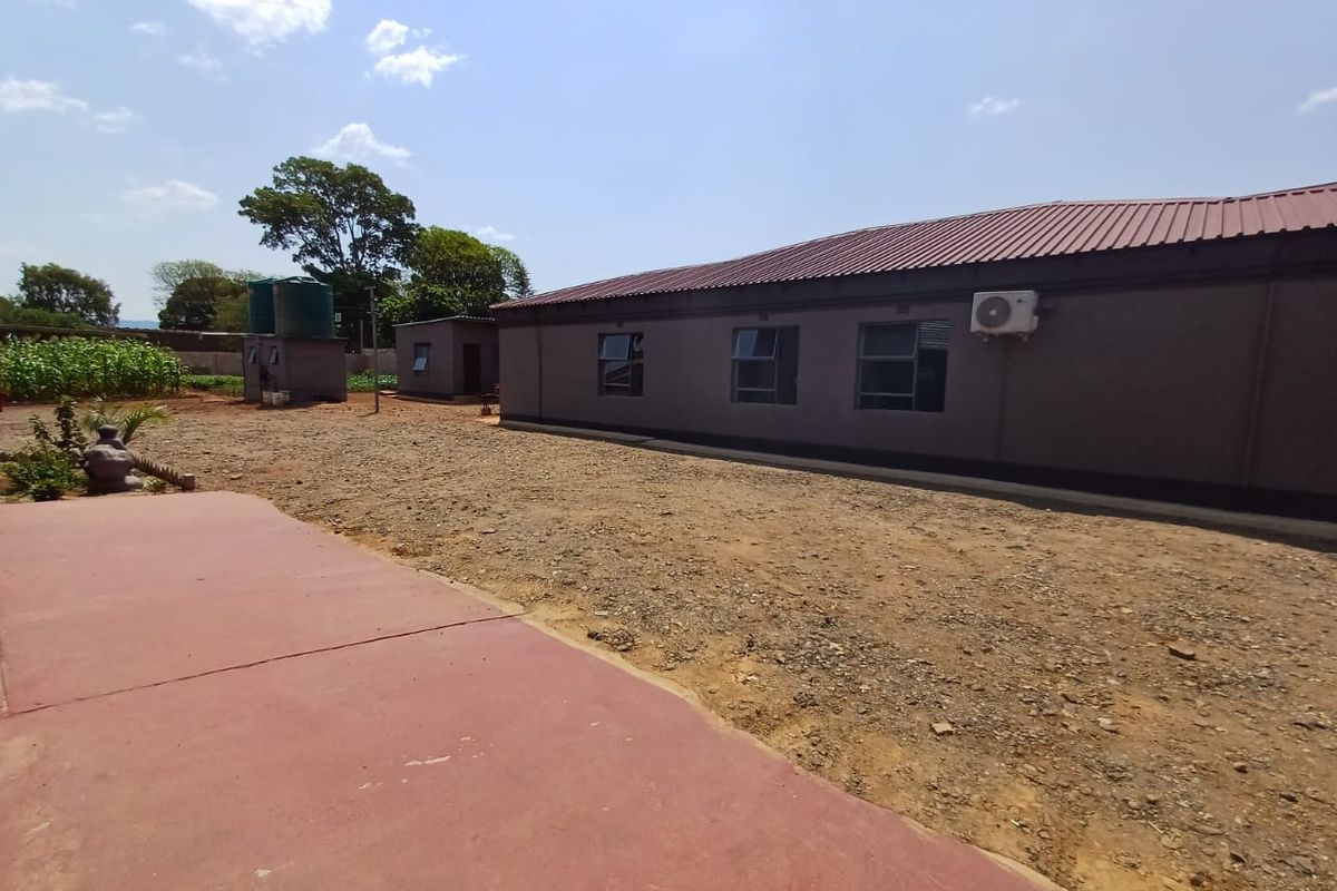Rear view of the industrial building featuring a corrugated metal roof, exterior air conditioning unit, and adjacent water storage tanks on an unpaved lot.
