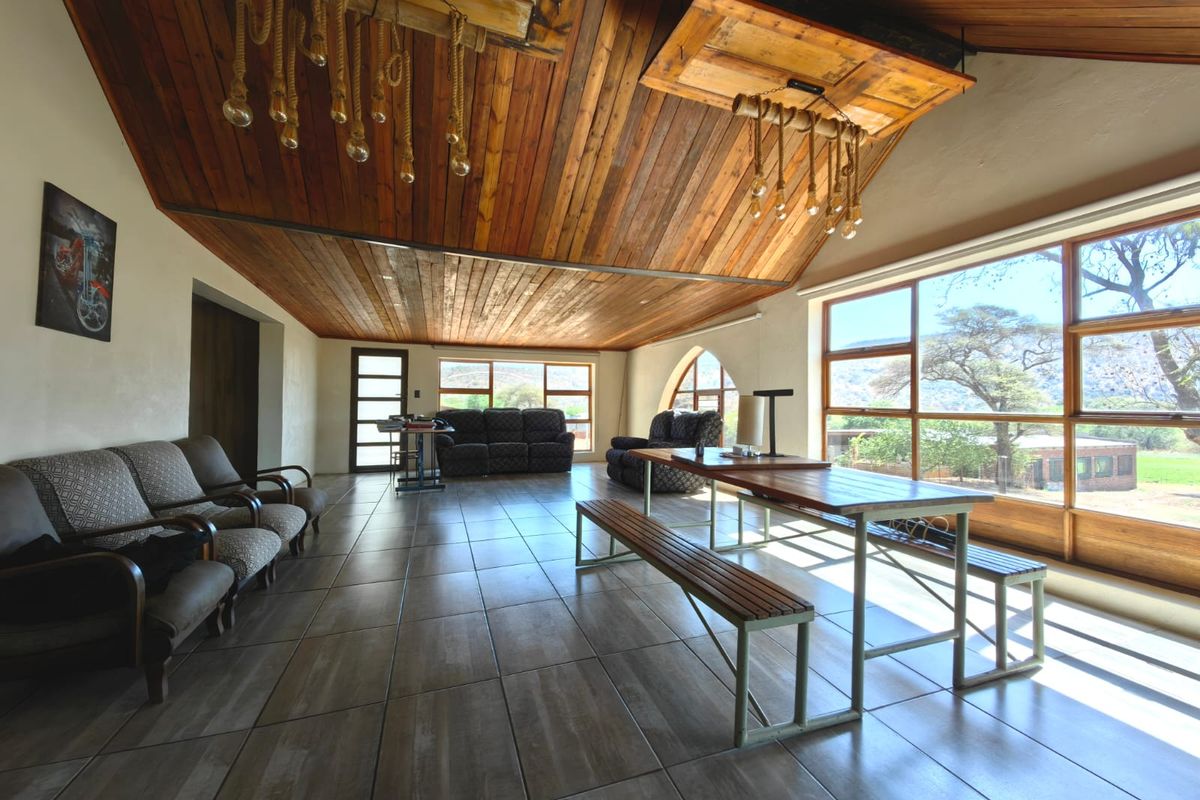 Spacious living area featuring a striking timber-clad vaulted ceiling, large format floor tiles, and expansive windows offering scenic views of the surrounding landscape.