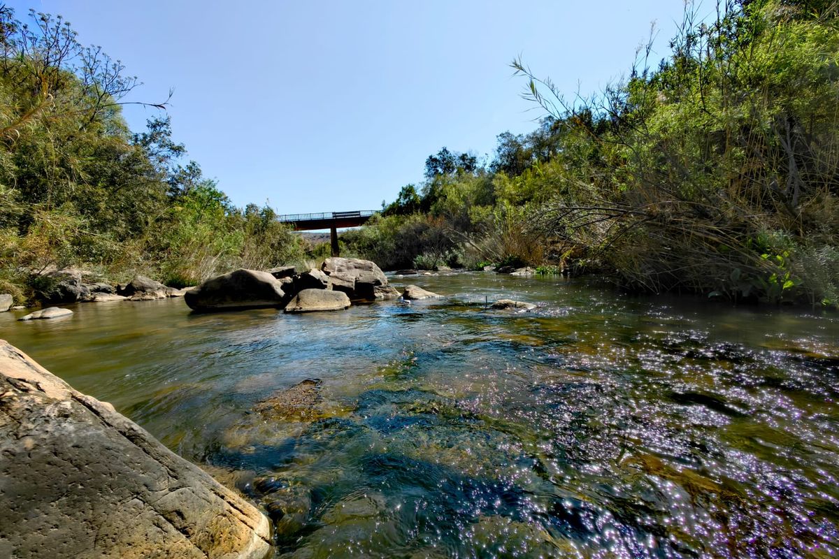 A scenic view of a natural river flowing through the farm property, featuring rock formations and a bridge in the distance.