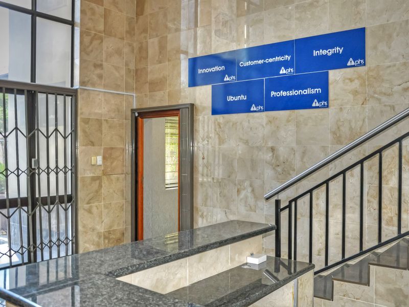 Professional office entry area featuring polished tiled wall cladding, a granite reception counter, and a secure metal staircase.