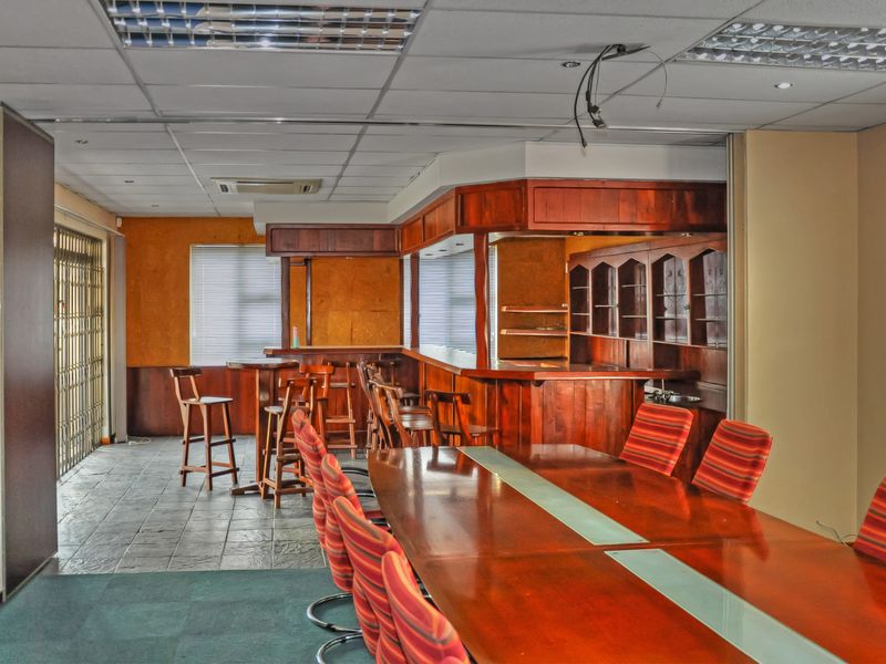 Office space featuring a built-in wooden bar area, mixed flooring, and suspended ceiling, offering potential for a modern corporate or social workspace renovation.