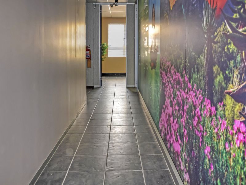 A functional office hallway featuring tiled flooring and a decorative wall mural, leading towards an adjacent office space.