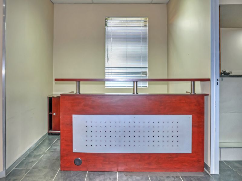 A professional office space featuring a built-in reception desk, tiled flooring, and a window with venetian blinds.