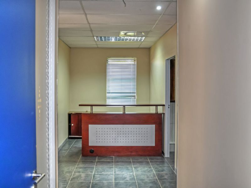 A vacant office space featuring a built-in reception desk, tiled flooring, and a suspended ceiling with recessed lighting.