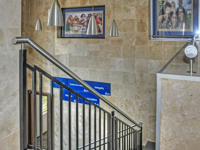 A modern office stairwell featuring elegant stone wall cladding, a sturdy metal railing, and contemporary pendant lighting.