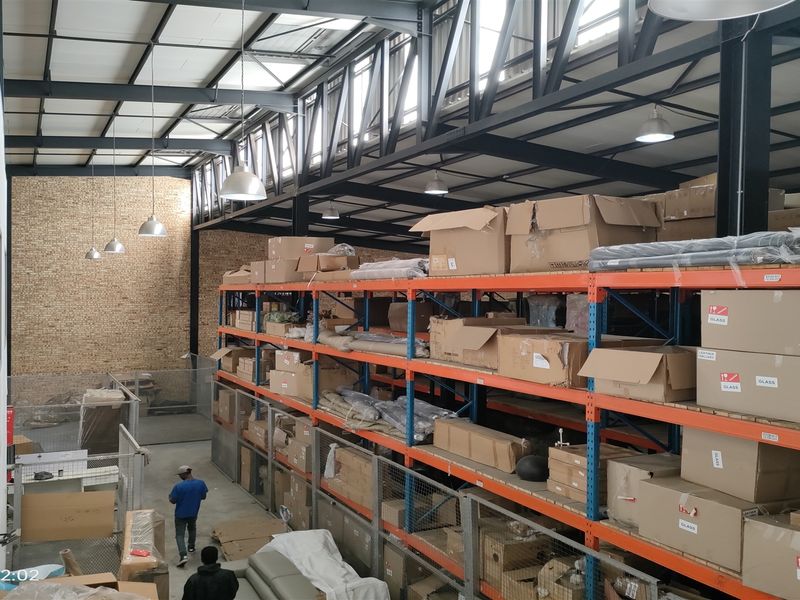 Spacious industrial warehouse featuring high ceilings with exposed steel trusses, extensive heavy-duty racking systems, and an exposed brick feature wall.