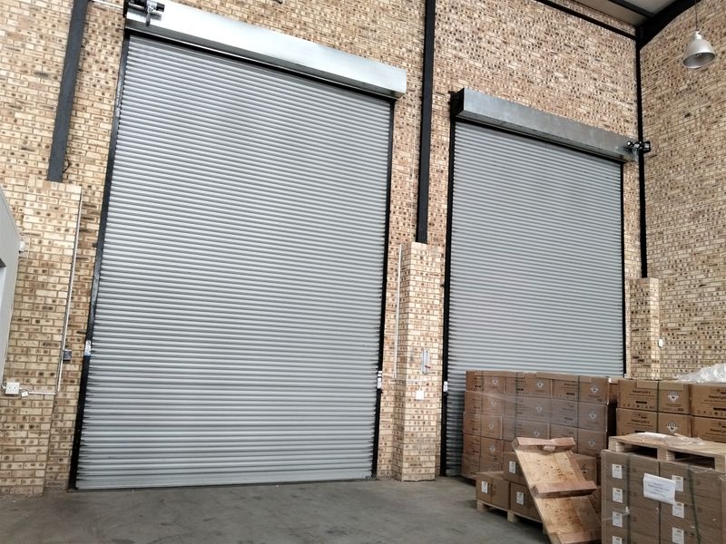 Industrial warehouse space featuring high-clearance roller shutter doors, exposed brickwork, and durable concrete flooring, suitable for logistics or storage operations.
