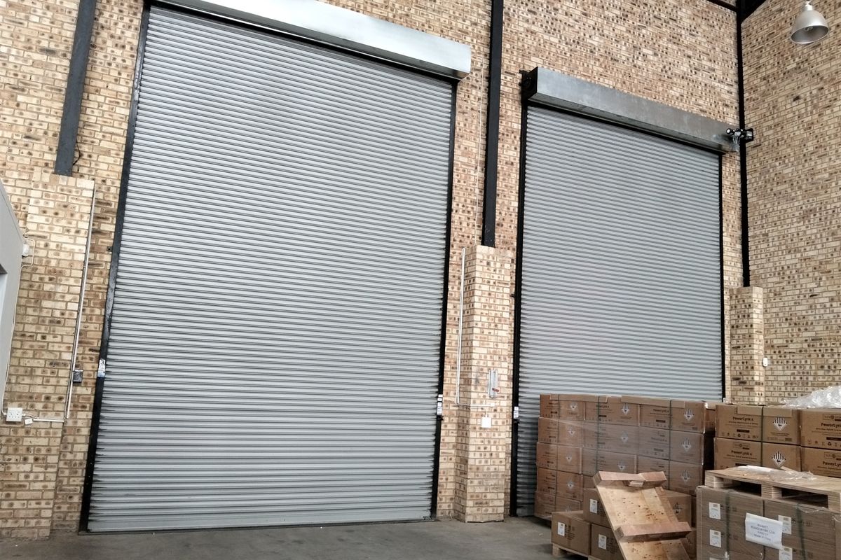 Industrial warehouse space featuring high-clearance roller shutter doors, exposed brickwork, and durable concrete flooring, suitable for logistics or storage operations.