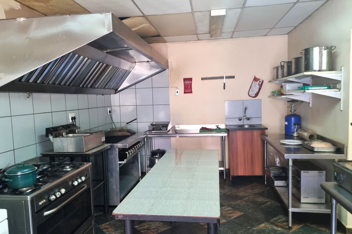 Commercial-style kitchen featuring a large extractor hood, gas stove, stainless steel prep surfaces, and tiled flooring, requiring some maintenance and cosmetic updates.
