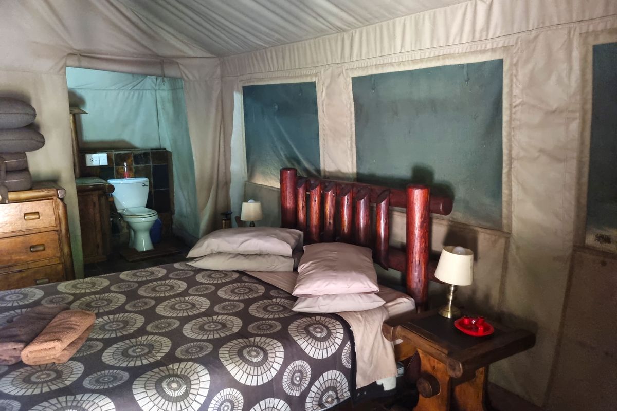 A rustic safari-style bedroom featuring canvas walls and an integrated en-suite bathroom area with a flush toilet.