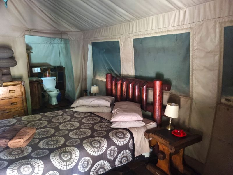 A rustic safari-style bedroom featuring canvas walls and an integrated en-suite bathroom area with a flush toilet.