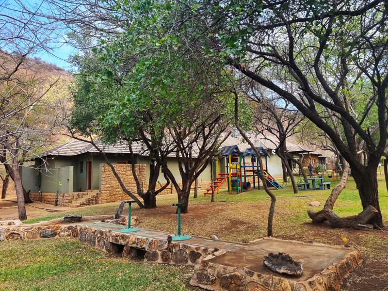 Rear view of the farm property featuring a stone-clad building, mature trees, and a landscaped garden area with a stone retaining wall.