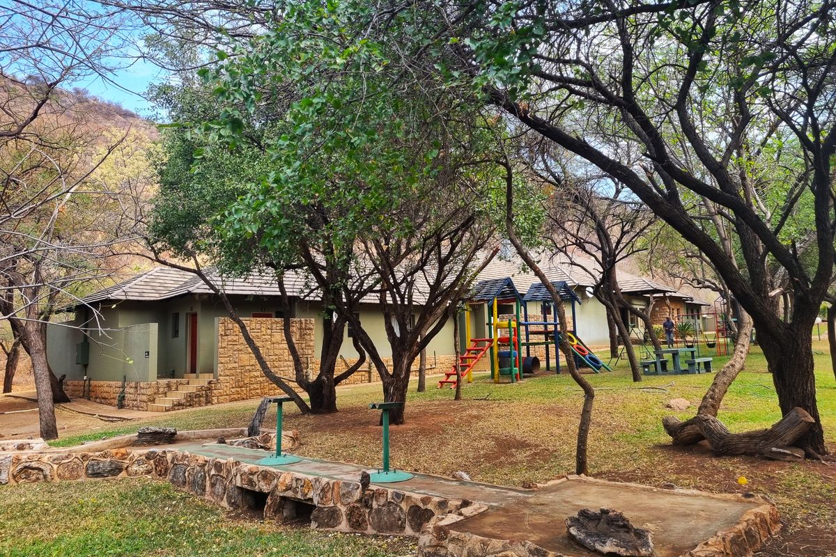 Rear view of the farm property featuring a stone-clad building, mature trees, and a landscaped garden area with a stone retaining wall.