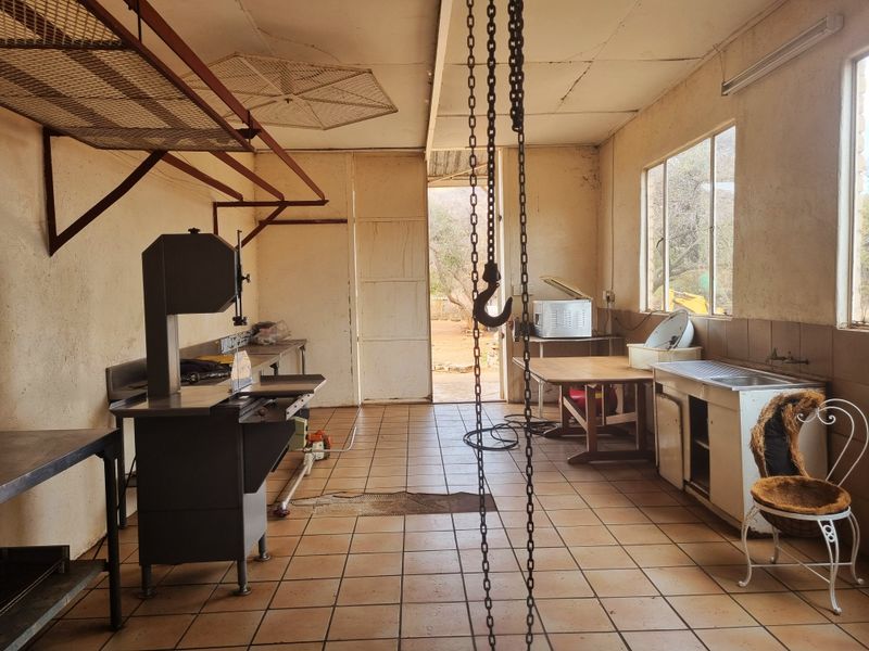 A functional utility or butchery workspace featuring tiled floors, a stainless steel sink, industrial equipment, and an overhead chain hoist for heavy lifting.