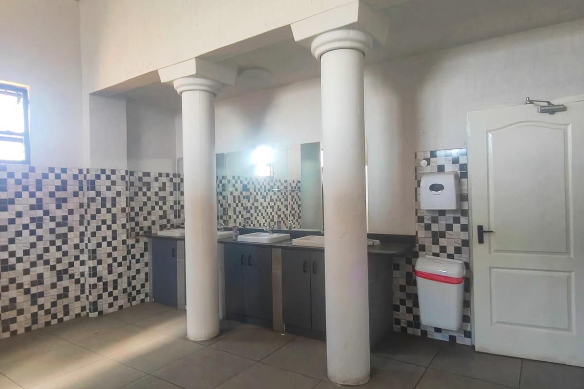 A functional commercial bathroom featuring tiled walls, double vanity basins, and structural columns.