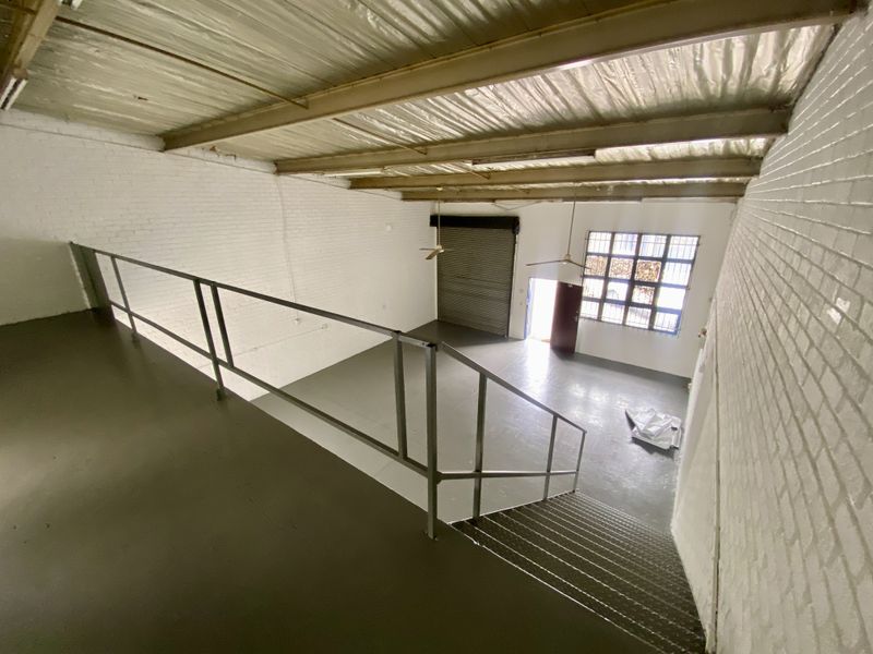 Spacious industrial open-plan unit featuring a mezzanine level, painted brick walls, exposed steel roof structure, and a large roller shutter door for easy access.