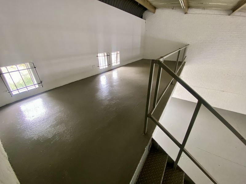 An elevated mezzanine level in an industrial space featuring painted brick walls, security-barred windows, and a metal staircase with safety railing.