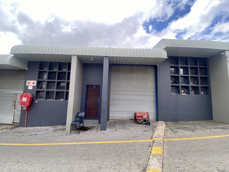 Industrial unit exterior featuring a roller shutter door, security gate, and grid windows with a fire hose reel installed on the facade.