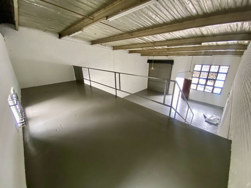 Spacious industrial mezzanine level featuring painted brick walls, exposed steel roof trusses, and a secure metal railing overlooking the main warehouse floor.