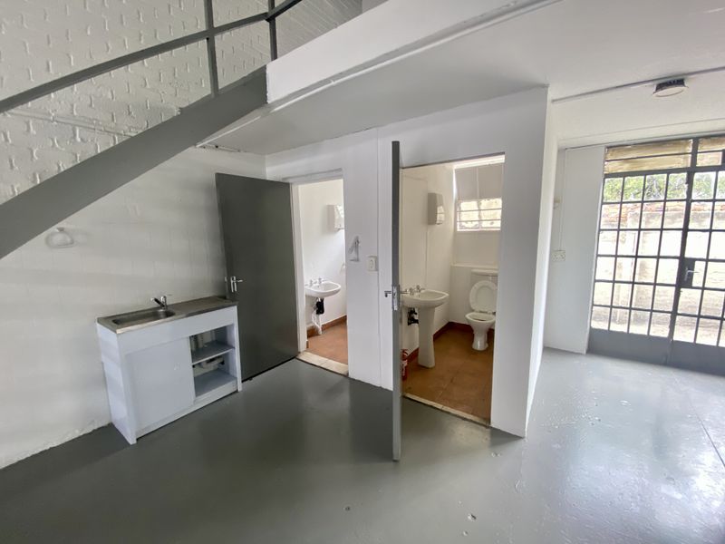 Industrial utility space featuring a kitchenette sink, two separate toilet cubicles with basins, and a metal staircase leading to an upper level.