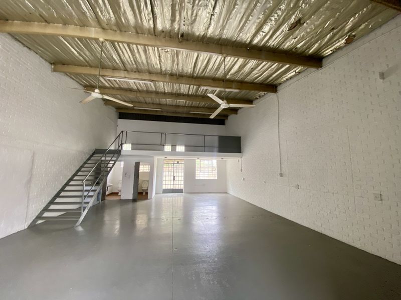 Spacious industrial open-plan unit featuring a mezzanine level, metal staircase, exposed roof structure, and painted brick walls with polished concrete flooring.
