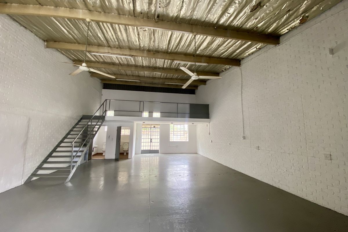 Spacious industrial open-plan unit featuring a mezzanine level, metal staircase, exposed roof structure, and painted brick walls with polished concrete flooring.