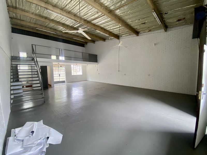 Spacious industrial open-plan unit featuring a mezzanine level, exposed steel roof structure, painted brick walls, and durable epoxy-coated concrete flooring.