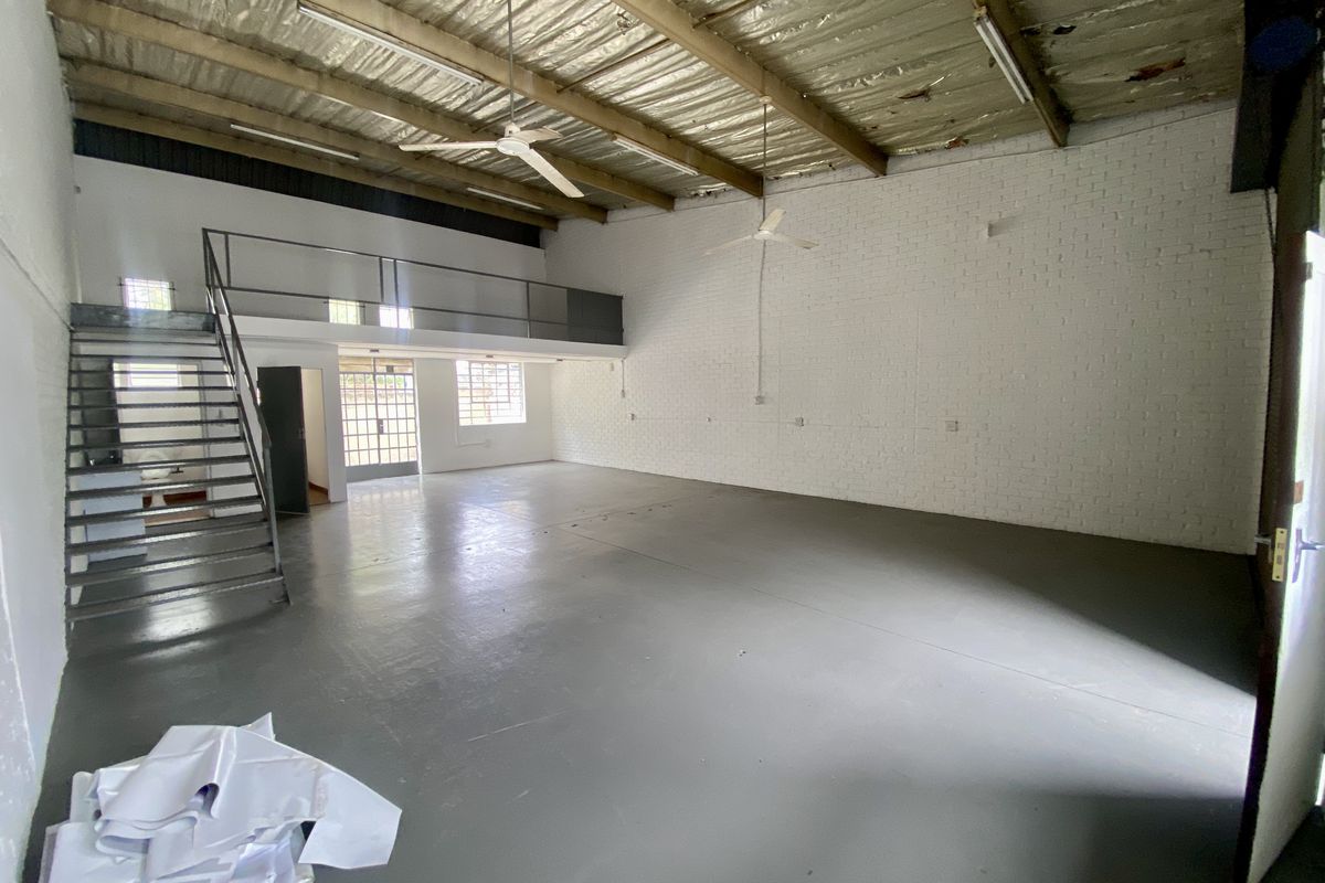 Spacious industrial open-plan unit featuring a mezzanine level, exposed steel roof structure, painted brick walls, and durable epoxy-coated concrete flooring.